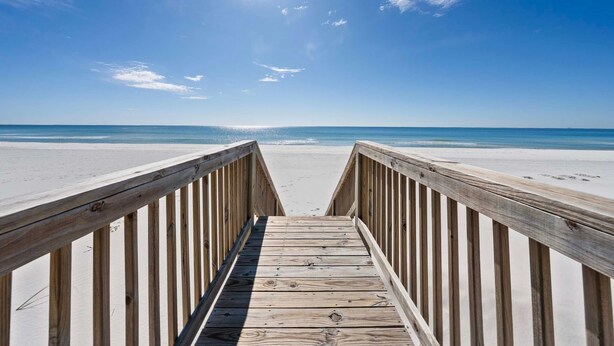 A wooden boardwalk leading to a beach with a clear sky and sun shining. - Far Reach II (Gulf Shores)