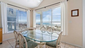 A dining area with a glass table and wicker chairs, large windows with blinds, and a ceiling fan. - Far Reach II (Gulf Shores)