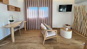 A modern living room with a wooden floor, a dining table with chairs, a sofa, a TV mounted on the wall, and a window with curtains. - Marinha Grande Apartamentos Rainbow N°9 (Marinha Grande)