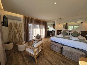 A modern hotel room with a large bed, a sitting area with a chair and ottoman, a wooden floor, and a view of the outside through the window. - Marinha Grande Apartamentos Rainbow N°9 (Marinha Grande)