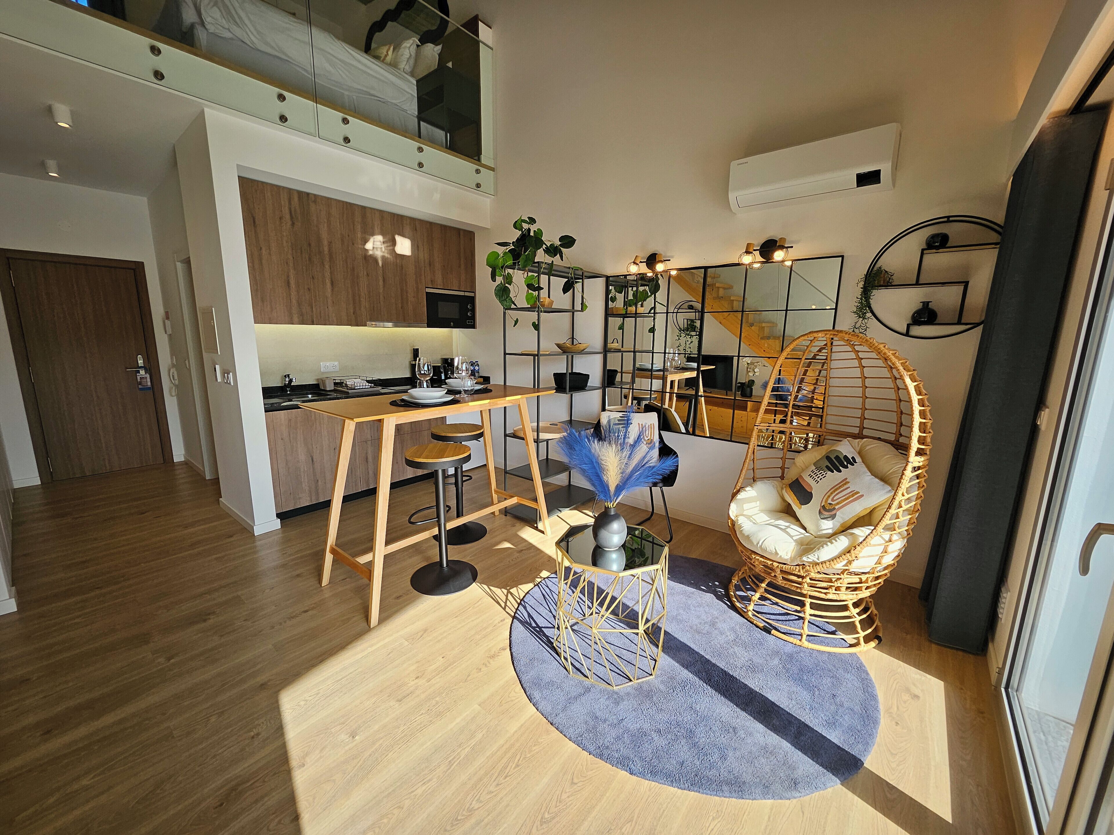 A modern apartment with a kitchen, dining area, and a living space with a hanging chair and a round table.