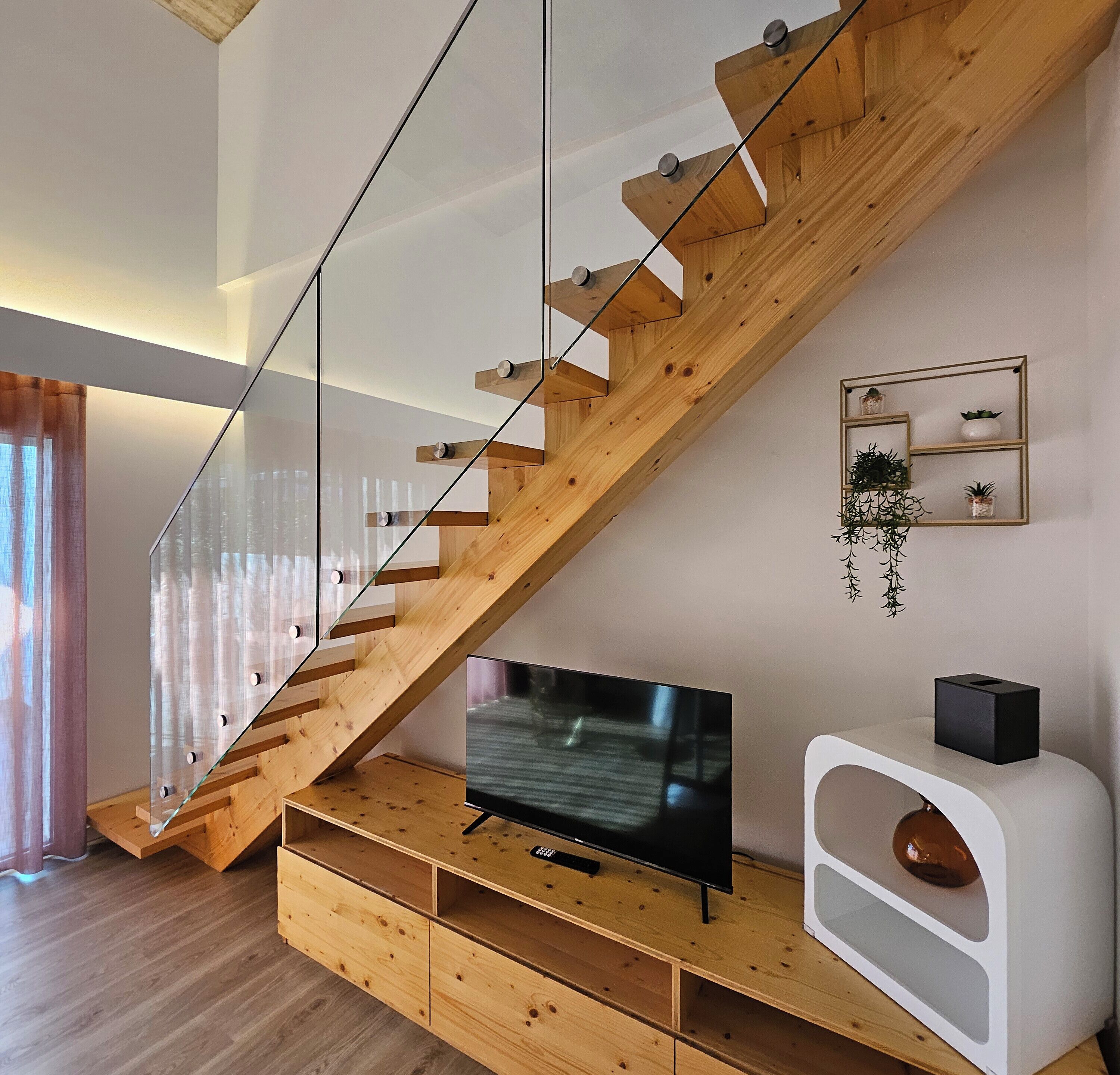 Ein modernes Wohnzimmer mit einer Holztreppe, einem Flachbildfernseher und einer weißen Unterhaltungsecke.