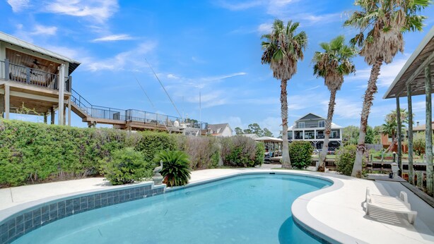 A swimming pool with a curved edge, surrounded by palm trees and a white deck with lounge chairs. - Fun In The Sun (Orange Beach)