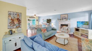 A living room with a sofa, a coffee table, and a fireplace. There is a television on a stand and a painting on the wall. - Fun In The Sun (Orange Beach)