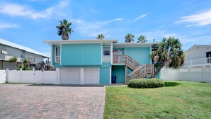 A two-story house with a blue exterior, a front porch, and a small front yard with a palm tree. - Fun In The Sun (Orange Beach)