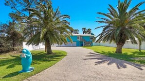 A pathway leading to a building with a blue door, surrounded by palm trees and a grassy area. - Fun In The Sun (Orange Beach)