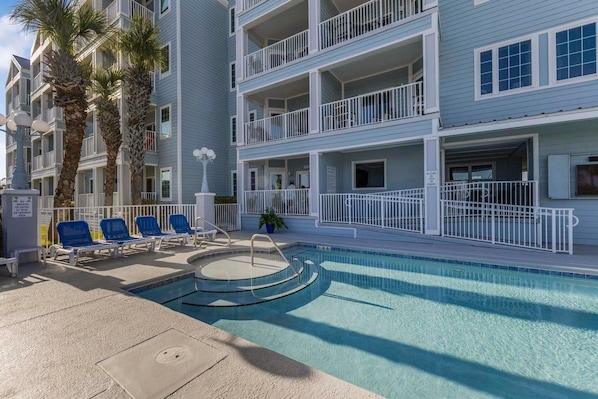 A pool area with blue chairs and a small pool, surrounded by a multi-story building with balconies.