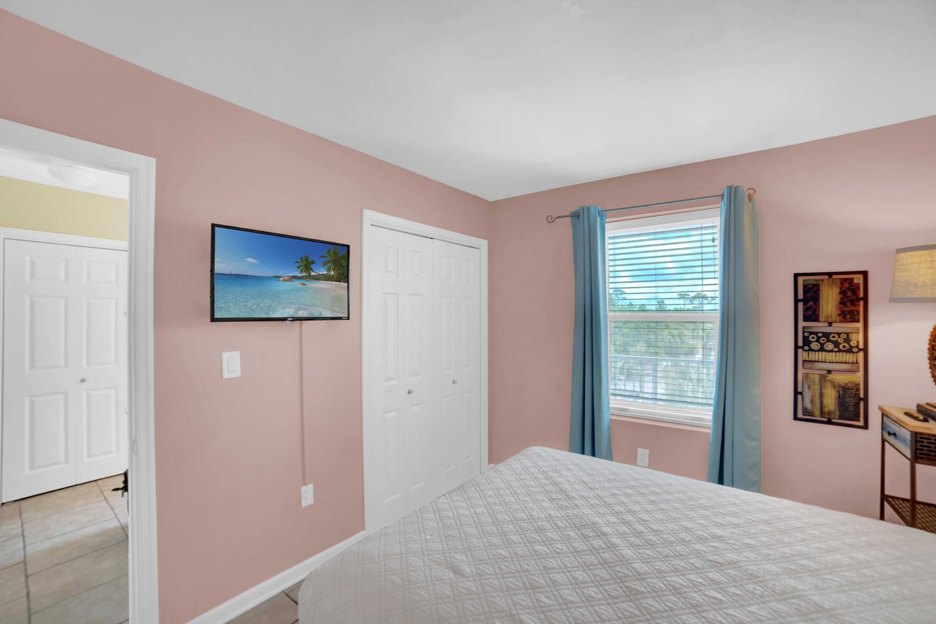 A bedroom with a bed, a TV mounted on the wall, a window with curtains, and a door.