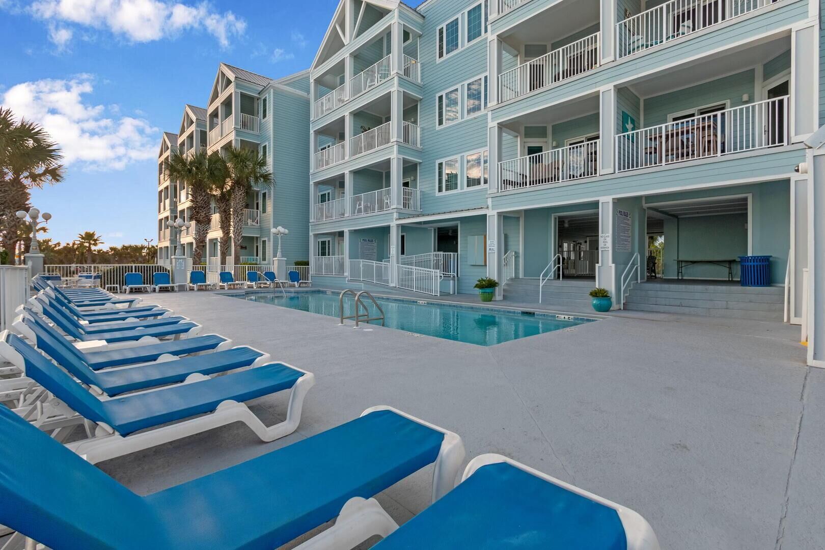 A poolside area with blue lounge chairs, a pool, and a multi-story building with balconies.