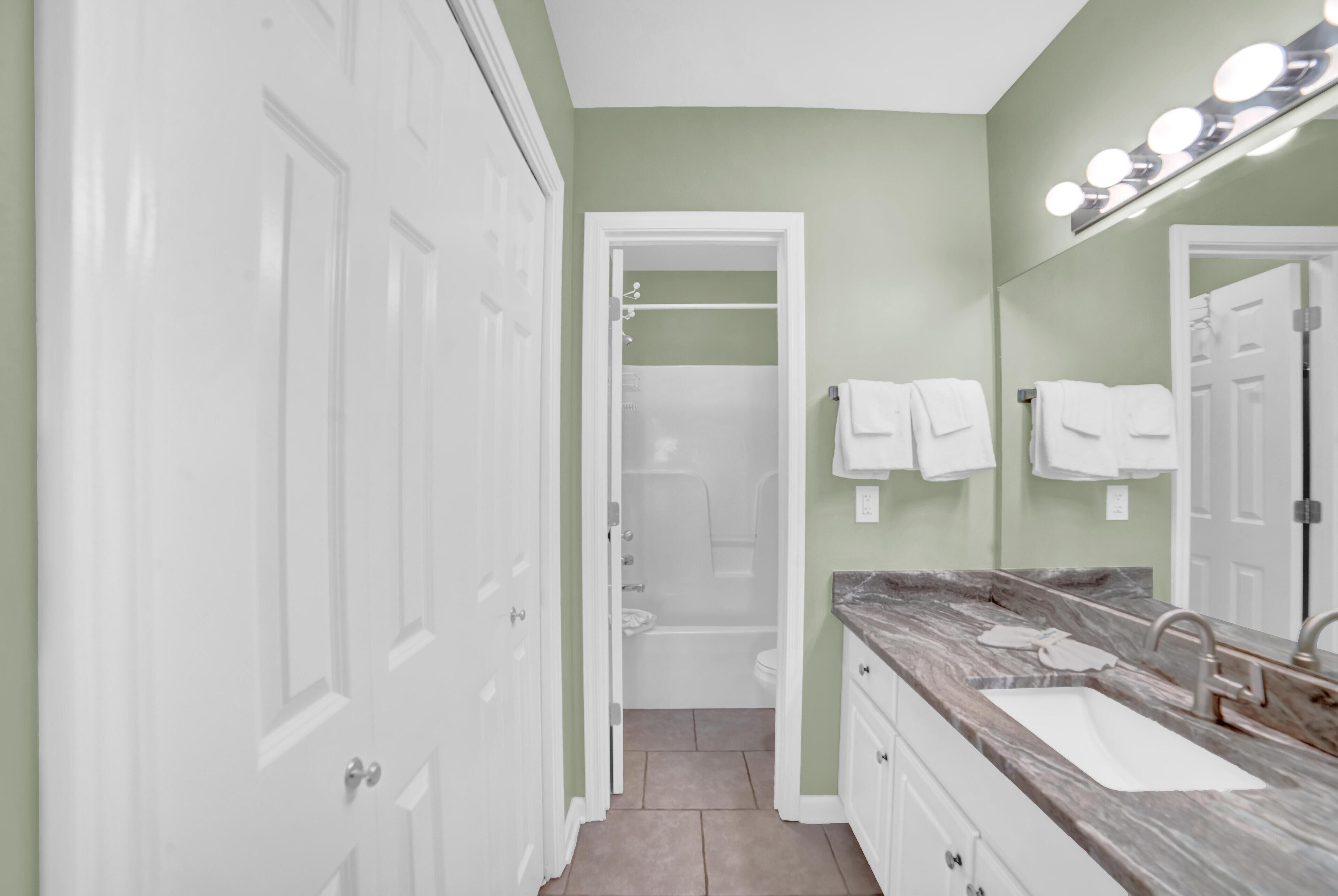 Un bagno con un mobile lavabo, un lavandino e uno specchio illuminato. Asciugamani bianchi sono appesi a un portasciugamani.