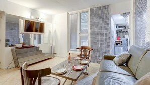 A modern living room with a sofa, dining table set for four, and a TV mounted on the wall. - Paris Maison Lombards Terrasse (Paris)