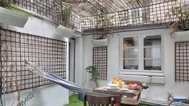 A small, enclosed outdoor space with a hammock, a table with a chair, and a window with decorative glass. - Paris Maison Lombards Terrasse (Paris)
