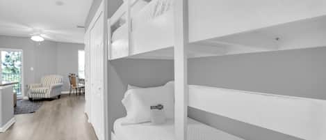 A room with bunk beds, a chair, a desk, and a view of the outdoors.