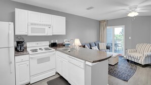 A modern kitchen with white appliances, a dining area with striped chairs, and a view to the outside. - Grand Caribbean 225 (Orange Beach)