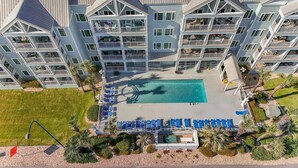 A multi-story hotel with a central swimming pool surrounded by lounge chairs and palm trees. - Grand Caribbean 225 (Orange Beach)