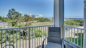 A balcony with a chair, overlooking a grassy area with trees and buildings in the distance. - Grand Caribbean 225 (Orange Beach)