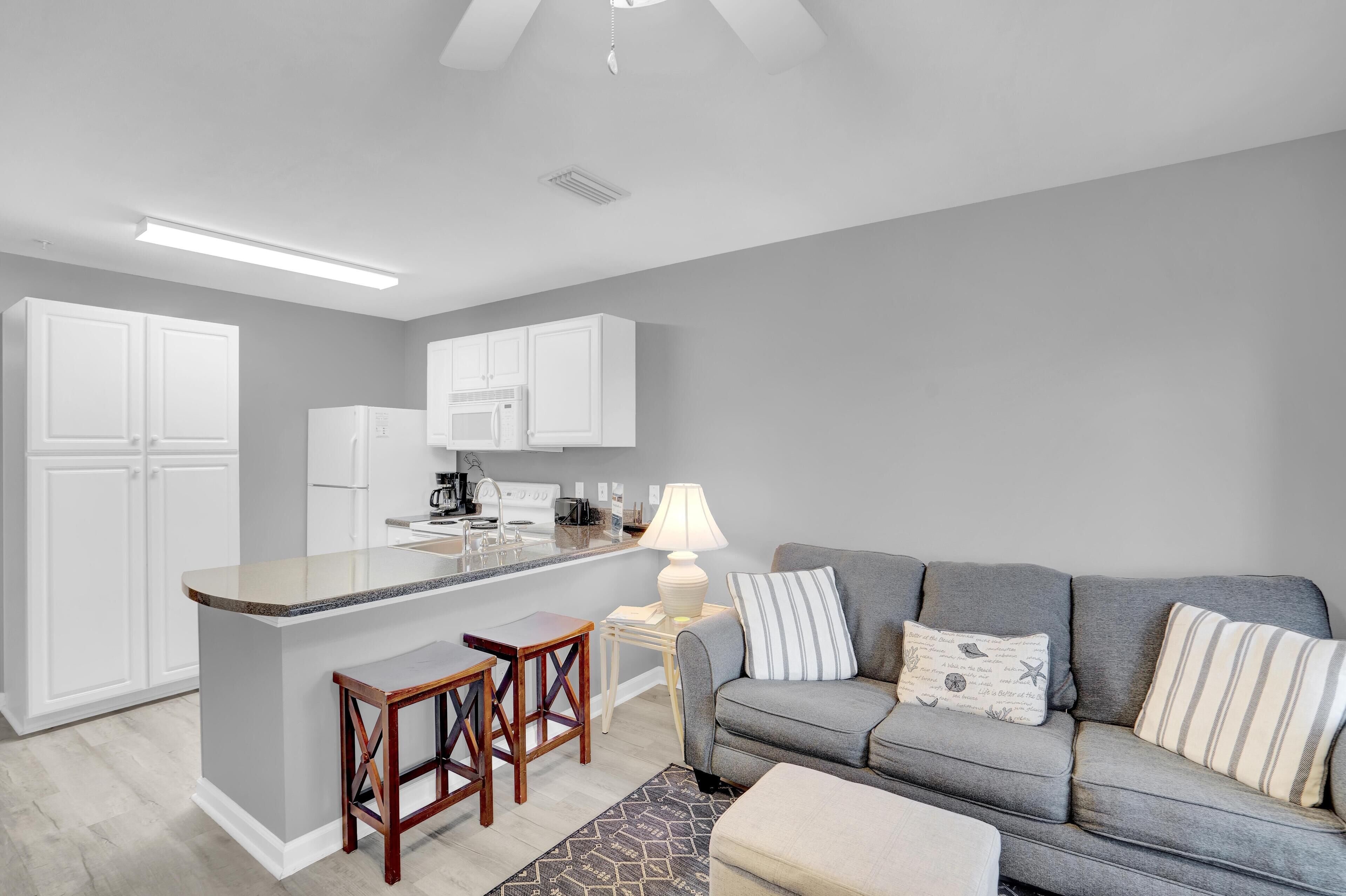A modern kitchen with white cabinets, a central island with stools, and a grey sofa with striped pillows.