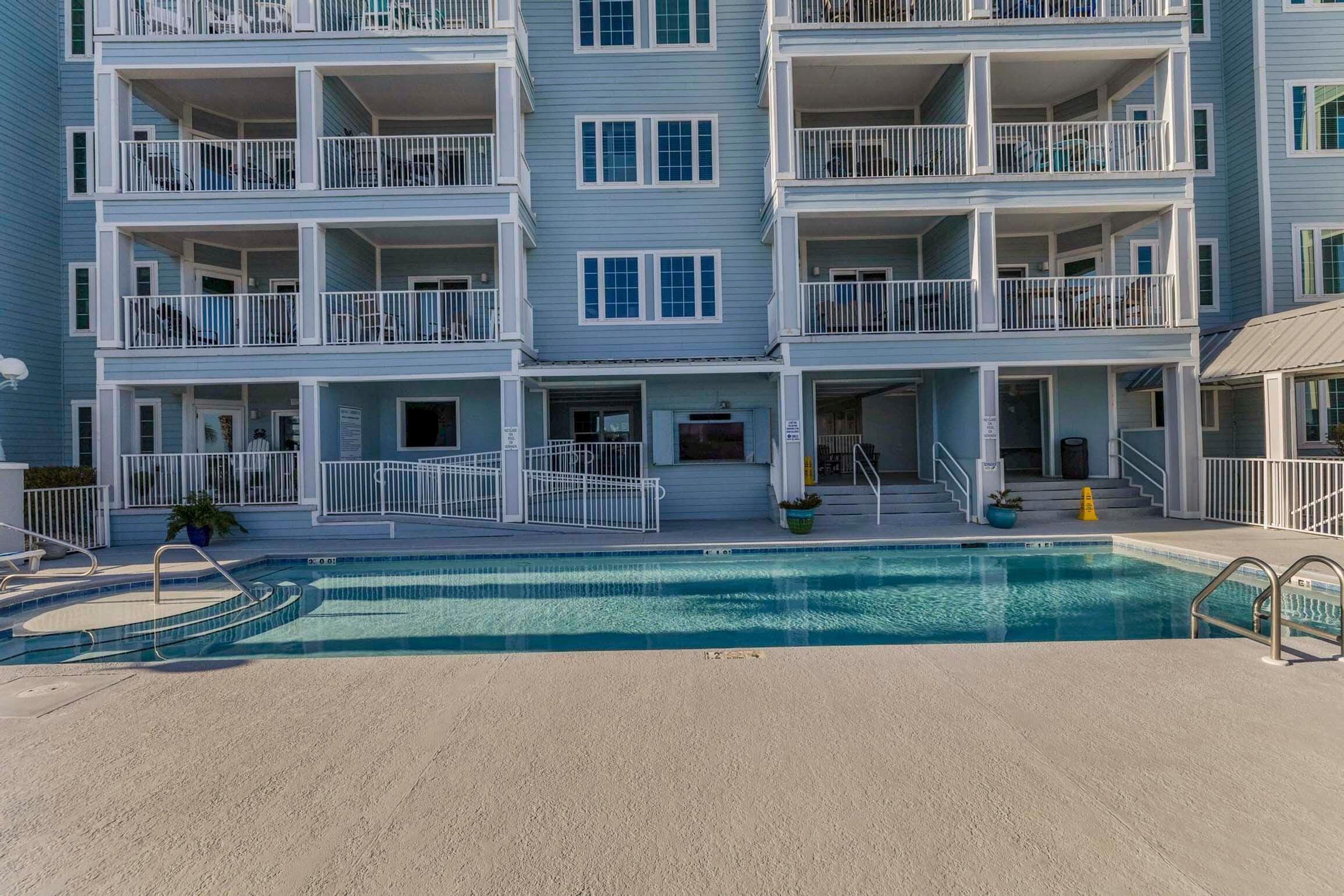 A multi-story building with balconies, a swimming pool, and a small outdoor area with steps leading to the pool.