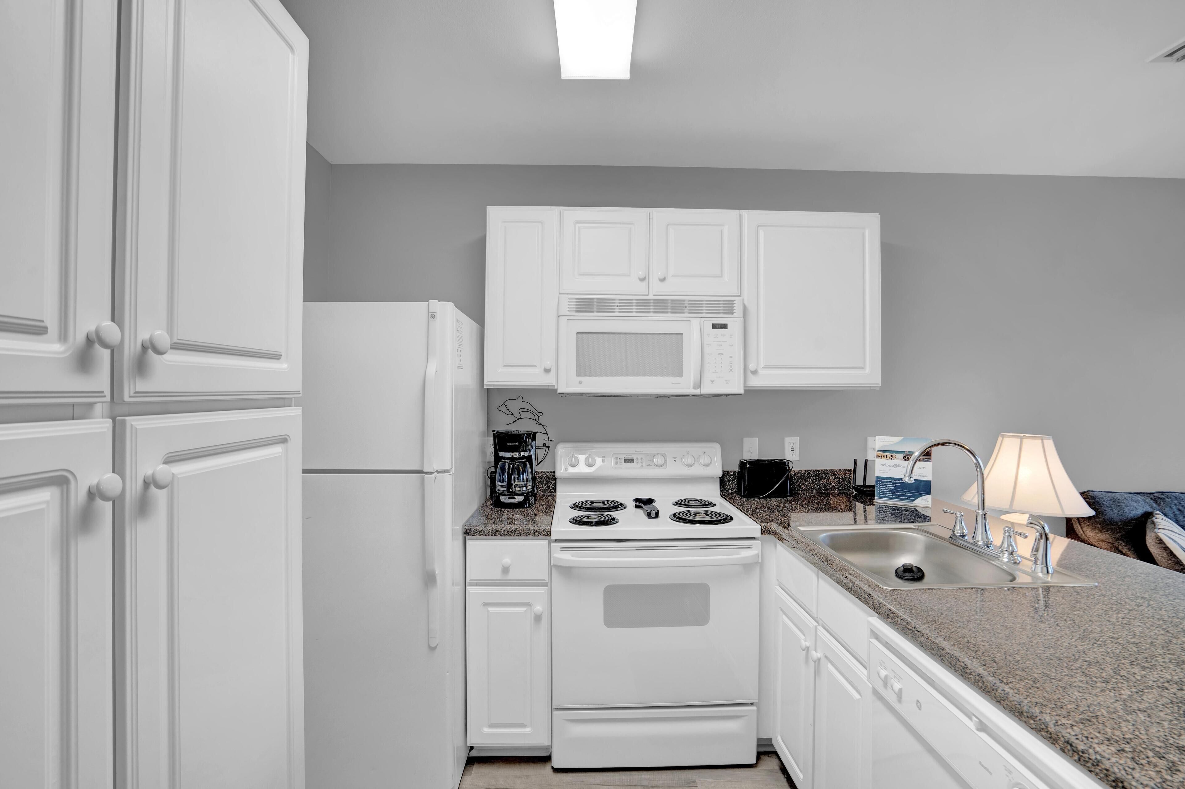 A kitchen with white cabinets, a stove, a microwave, and a sink.