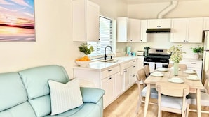 Una cocina moderna con armarios blancos, una mesa de comedor preparada para cuatro personas y un sofá azul claro con un cojín estampado.