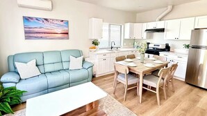 Una cocina moderna con armarios blancos, una mesa de comedor con sillas, un sofá azul y una mesita de centro blanca.