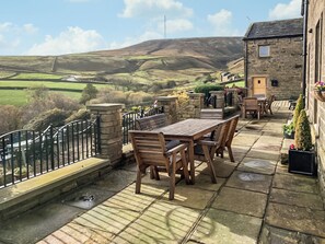 A patio with a stone table and chairs, a stone wall, and a view of rolling hills.