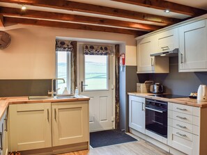 A kitchen with wooden beams, a sink, cabinets, a stove, and a view through a door.