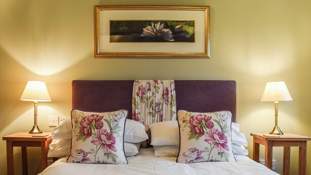 Et hotelværelse med en seng, to sengeborde med lamper, et blomsterbillede over sengen og et blomstret gardin.
