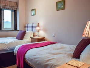 A hotel room with two beds, a window with curtains, a bedside lamp, and a wall-mounted light switch.