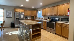 A modern kitchen with wooden cabinets, stainless steel appliances, and a central island with bar stools. - Soundside Home in Frisco is an Island Dream Retreat! (FRISCO)