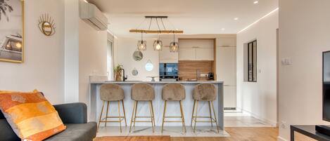 Un salon moderne comprenant un canapé, une table basse et un coin cuisine avec des tabourets de bar.