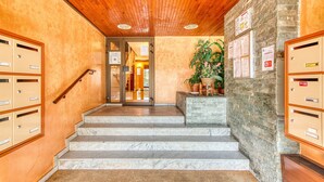 Eine Treppe führt zu einem Raum mit Holzboden und Steinwänden, begleitet von Briefkästen und einer Topfpflanze.