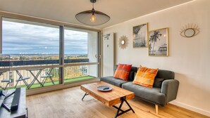 Ein modernes Wohnzimmer mit einem großen Fenster, einem grauen Sofa und einem Holztisch.