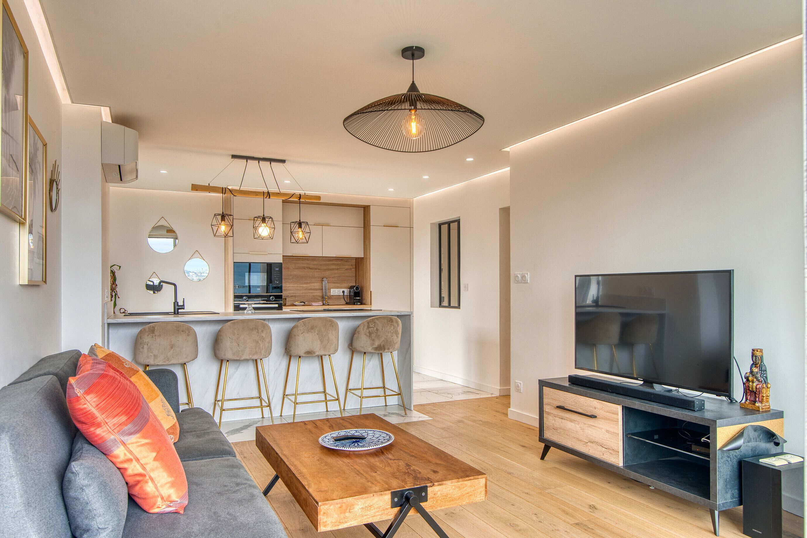 Una sala de estar moderna con un sofá, una mesa de centro, un televisor y una cocina al fondo.