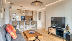 Ein modernes Wohnzimmer mit Sofa, Couchtisch, Fernseher und einer Küche im Hintergrund.