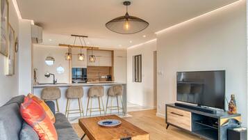 Una sala de estar moderna con un sofá, una mesa de centro, un televisor y una cocina al fondo.