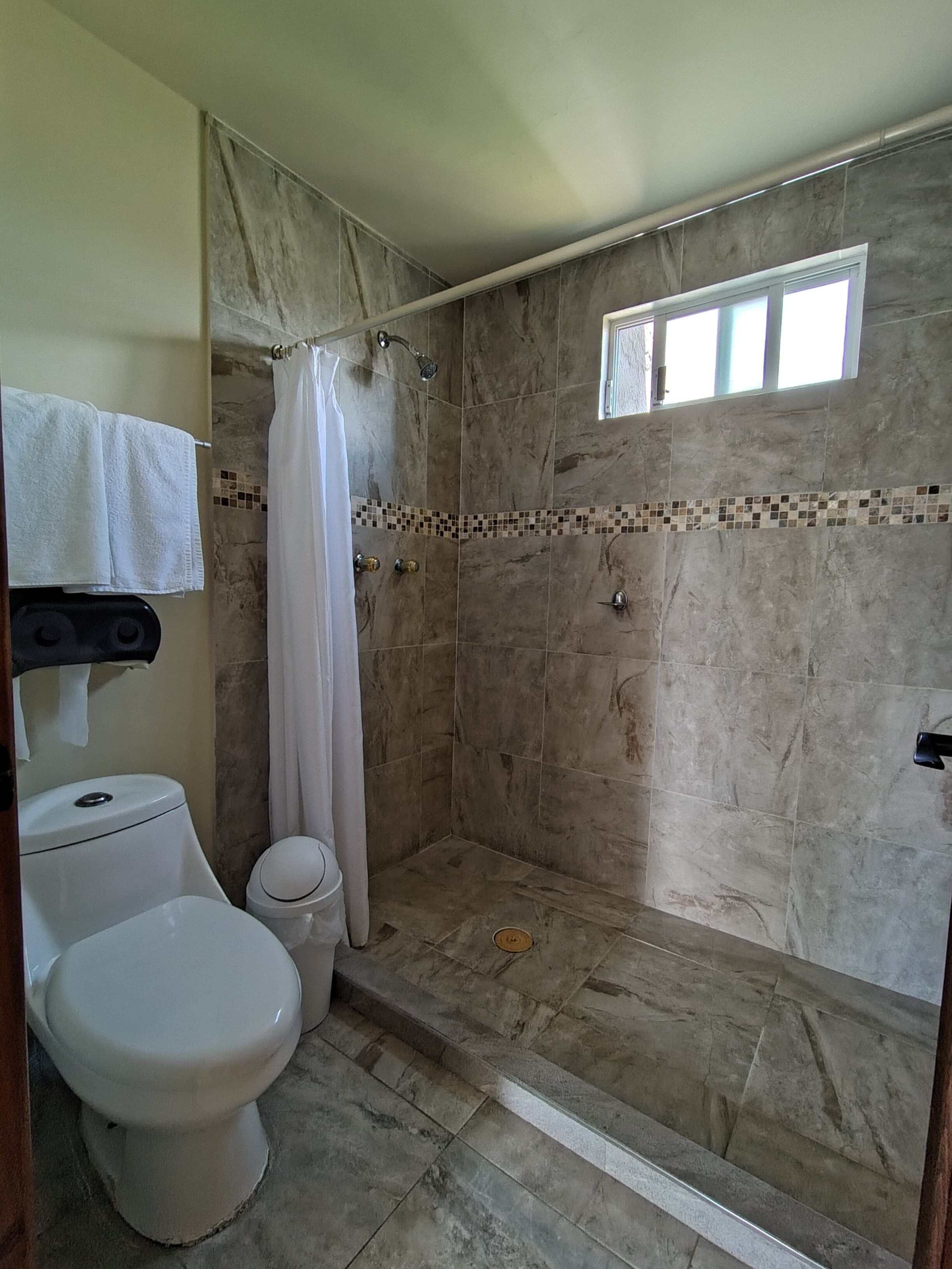 Un baño con ducha, inodoro y un pequeño ventanal.
