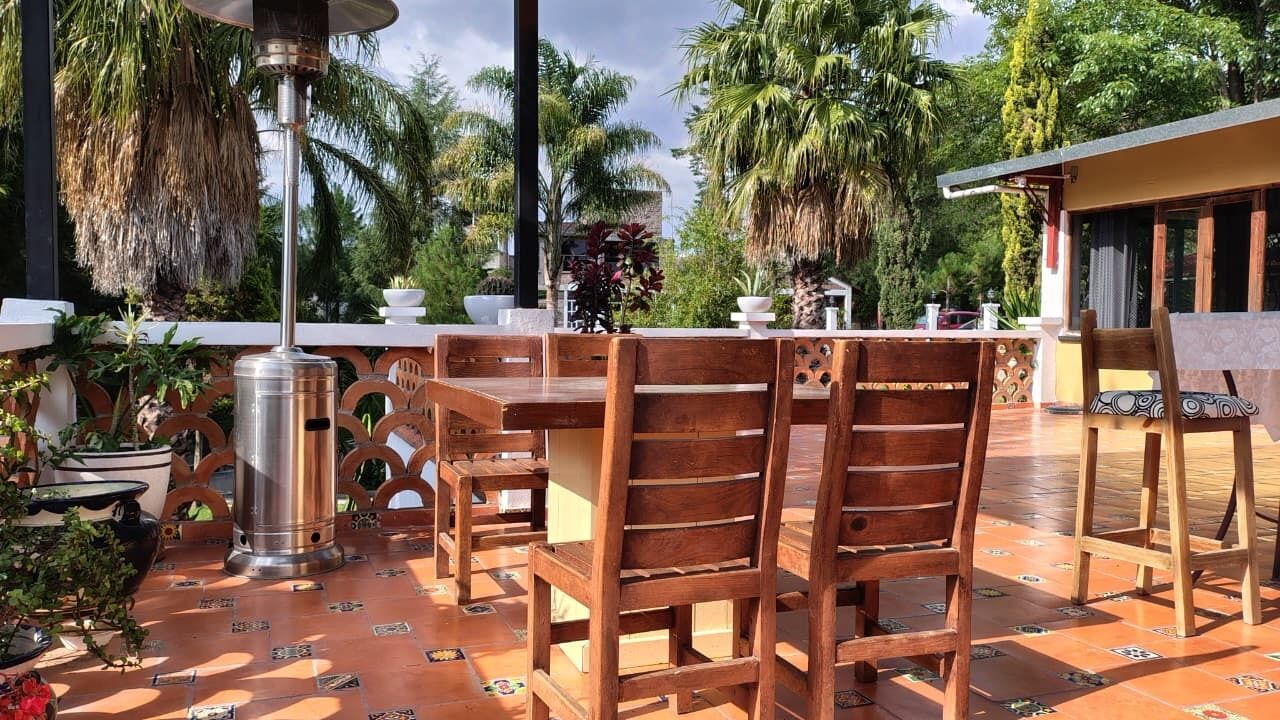 An outdoor patio with wooden tables and chairs, a metal heater, and potted plants.