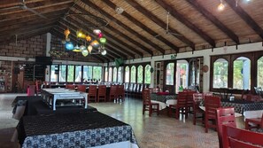 A spacious indoor dining area with high ceilings, wooden beams, and large windows. Tables are arranged for dining, and there are chairs and tables set up for guests. - HOTEL XIADANI  temazcal y SPA (Tlaxcala)