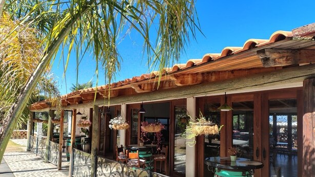 Ein Restaurant mit Außenbereich, überdacht mit einem Holzdach und von Palmen gesäumt.