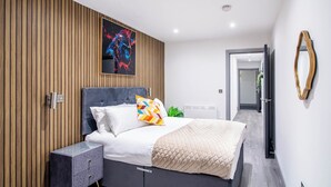 A modern bedroom with a bed, nightstands, a wall-mounted mirror, and a ceiling light fixture.