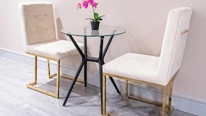 A room with two white upholstered chairs, a glass table with a black base, and a potted orchid.