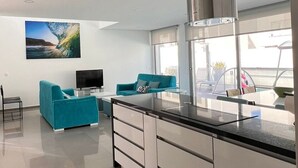 A modern kitchen with a large island, two blue sofas, a flat-screen TV, and a large window with a view of the outdoors. - Silvercoast Villa Concha Baia - private heated pool and rooftop seaview lounge. (Salir do Porto)
