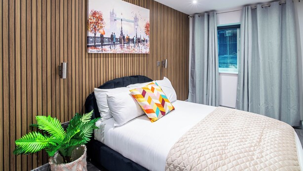 Una habitación de hotel moderna con una cama grande, un panel de pared de madera, un cuadro de un paisaje urbano y una ventana con cortinas.