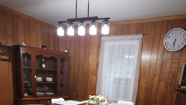 Une salle à manger aux murs lambrissés, avec une longue table, des chaises, une horloge et un buffet aux portes vitrées.