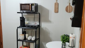 Une cuisine compacte équipée d’un four à micro-ondes, d’une machine à café et d’étagères contenant des ustensiles de cuisine. On y trouve une petite table agrémentée d’une plante et d’une bougie.