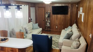 Un salon chaleureux avec un plancher en bois, un canapé blanc, un fauteuil bleu et un téléviseur fixé au mur.