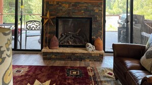 A cozy living room with a stone fireplace, leather couch, and a large TV.