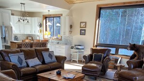 A spacious living room with leather sofas, a coffee table, and a large window with a view of trees.