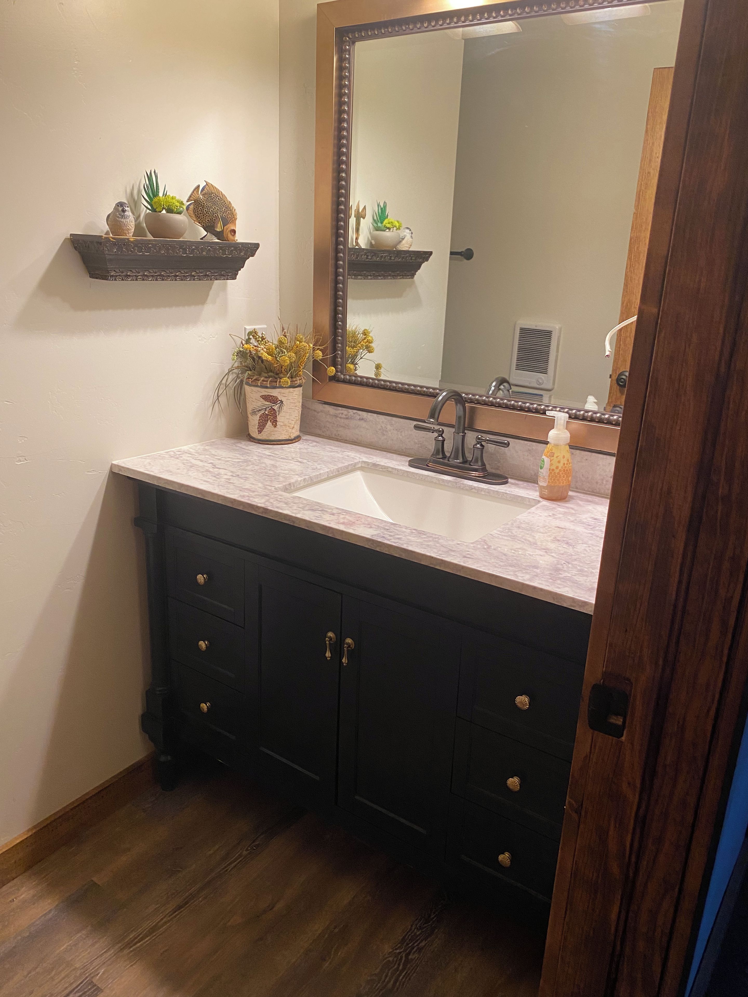 A bathroom with a marble sink, dark wooden cabinets, and decorative items on a shelf.
